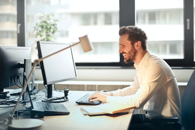 Smiling person in a white button down shirt using a desktop computer at their desk